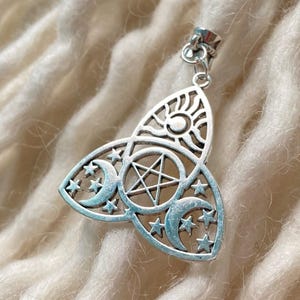 Op de afbeelding: Zilverkleurige hanger met een hemels ontwerp. De hanger toont een zon, halve manen, sterren en een pentagram in een driehoekige vorm. De hanger is opgehangen aan een kleine lus.