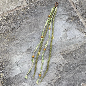 Peut inclure: Un accessoire pour cheveux vert et beige avec des perles en bois et des accents de feuilles. L'accessoire a une boucle marron en haut pour l'attache. Les brins sont décorés de petites feuilles vertes et de perles en bois.