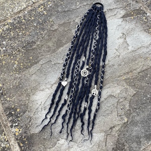 May include: Dark blue dreadlocks with silver accents and charms. The dreadlocks are adorned with silver charms in the shape of a heart, a pentagram, and a tree of life. The dreadlocks are tied together with a black hair tie.