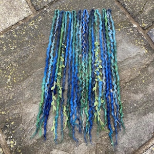 May include: A set of blue, green, and teal dreadlocks with silver accents and green leaf accents. The dreadlocks are arranged in a vertical pattern, with varying shades of blue and green.
