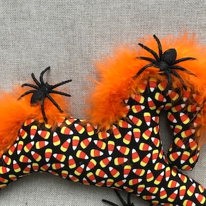 May include: A black and orange Halloween horse with a candy corn pattern and three black spiders. The horse is made of fabric and has orange feathers.