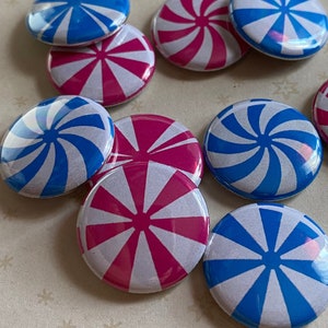 May include: A collection of eight round pinback buttons with a peppermint swirl design. Half of the buttons are blue and white, and the other half are pink and white.