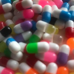 May include: A large collection of colorful capsules with white tops. The capsules are made of plastic and are in various colors, including red, blue, green, yellow, orange, and purple.