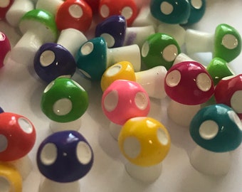Op de afbeelding: Een verzameling kleurrijke miniatuur paddenstoelfiguren met witte stippen. De paddenstoelen zijn gemaakt van plastic en hebben een verscheidenheid aan kleuren, waaronder rood, groen, blauw, geel en roze.