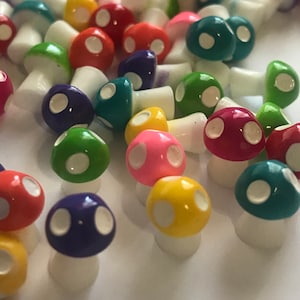 May include: A collection of colorful miniature mushroom figurines with white polka dots. The mushrooms are made of plastic and have a variety of colors, including red, green, blue, yellow, and pink.