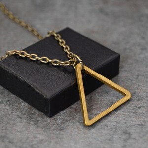 May include: A gold chain necklace with a large, open triangle pendant. The pendant is made of thick, polished metal and hangs from a simple chain.