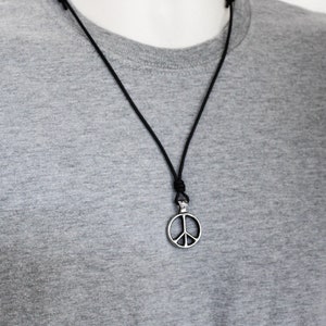 Peut inclure: Un collier en cordon de cuir noir avec un pendentif en argent en forme de signe de paix.