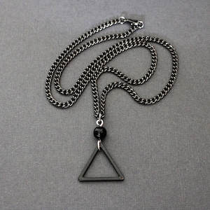 May include: A black chain necklace with a black triangle pendant and a black bead.
