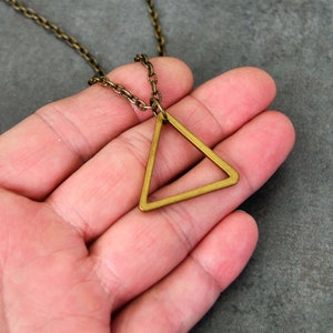 Peut inclure: Un collier avec un pendentif en forme de triangle dor&eacute; au design g&eacute;om&eacute;trique simple. Le pendentif est suspendu &agrave; une cha&icirc;ne d&eacute;licate.