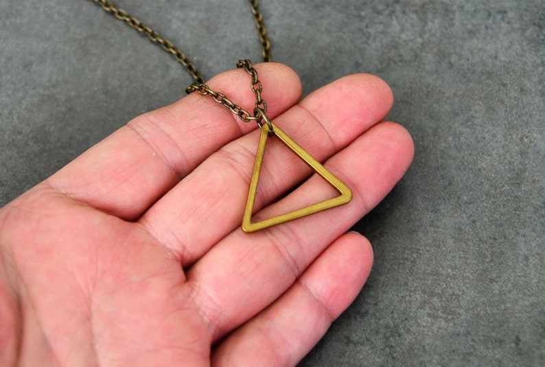 Peut inclure: Un collier avec un pendentif en forme de triangle dor&eacute; au design g&eacute;om&eacute;trique simple. Le pendentif est suspendu &agrave; une cha&icirc;ne d&eacute;licate.
