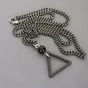 May include: A black chain necklace with a black triangle pendant and a black bead.