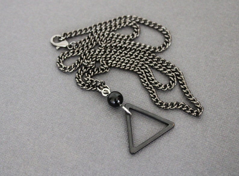 May include: A black chain necklace with a black triangle pendant and a black bead.