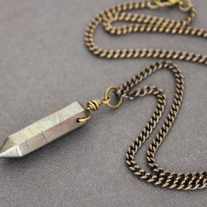 May include: A gold chain necklace with a long, pointed, grey and brown crystal pendant.