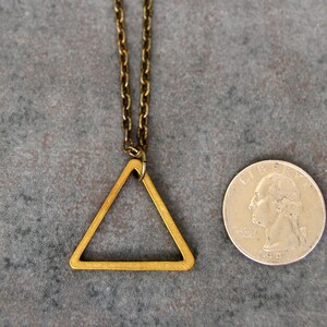 Peut inclure: Un collier avec un pendentif en forme de triangle dor&eacute;, au design g&eacute;om&eacute;trique simple. Le pendentif est &agrave; peu pr&egrave;s de la taille d'une pi&egrave;ce de 25 centimes d'euro.