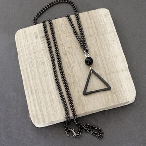 May include: A black chain necklace with a black triangle pendant. The pendant has a black bead at the top.