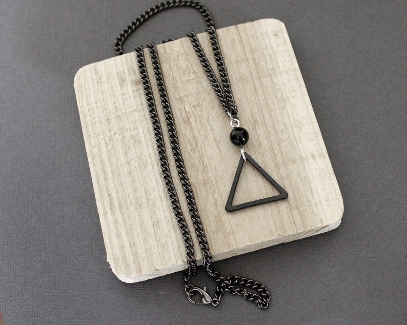May include: A black chain necklace with a black triangle pendant. The pendant has a black bead at the top.