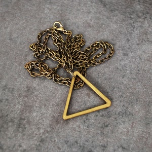 Peut inclure: Un collier en cha&icirc;ne dor&eacute;e avec un pendentif triangulaire. Le pendentif est en m&eacute;tal et a un design simple et g&eacute;om&eacute;trique.