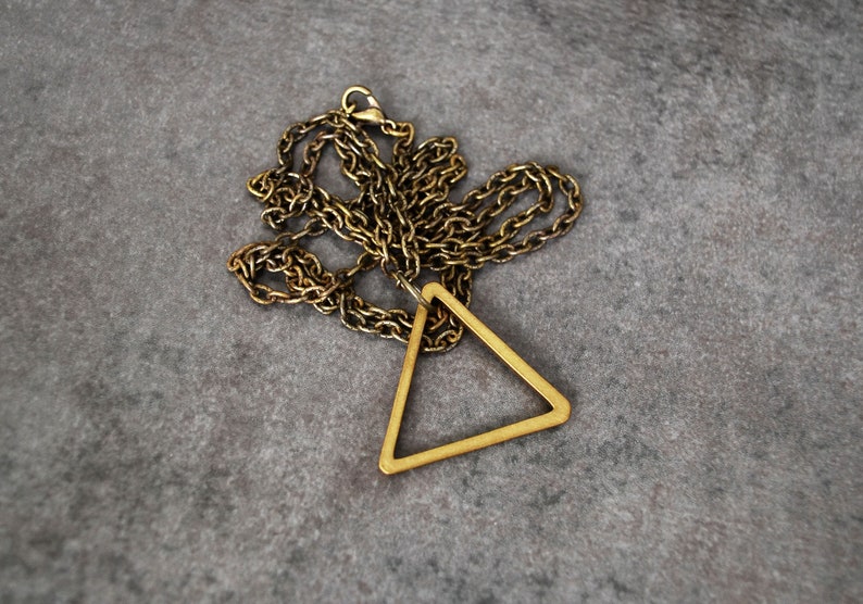 Peut inclure: Un collier en cha&icirc;ne dor&eacute;e avec un pendentif triangulaire. Le pendentif est en m&eacute;tal et a un design simple et g&eacute;om&eacute;trique.