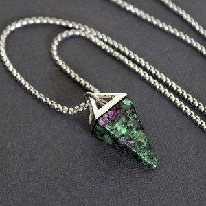 May include: A silver-toned necklace featuring a pendant with a triangular, faceted gemstone. The gemstone has a mix of green and pink hues. The chain is a fine, textured design.