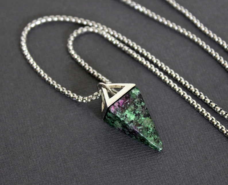 May include: A silver-toned necklace featuring a pendant with a triangular, faceted gemstone. The gemstone has a mix of green and pink hues. The chain is a fine, textured design.