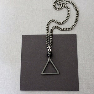 May include: A silver chain necklace with a black triangle pendant and a black bead.