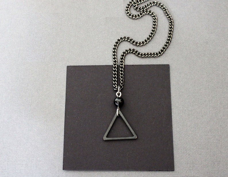May include: A silver chain necklace with a black triangle pendant and a black bead.