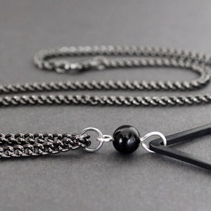 May include: A black chain necklace with a black triangle pendant and a black bead.