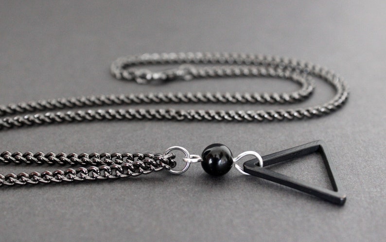 May include: A black chain necklace with a black triangle pendant and a black bead.