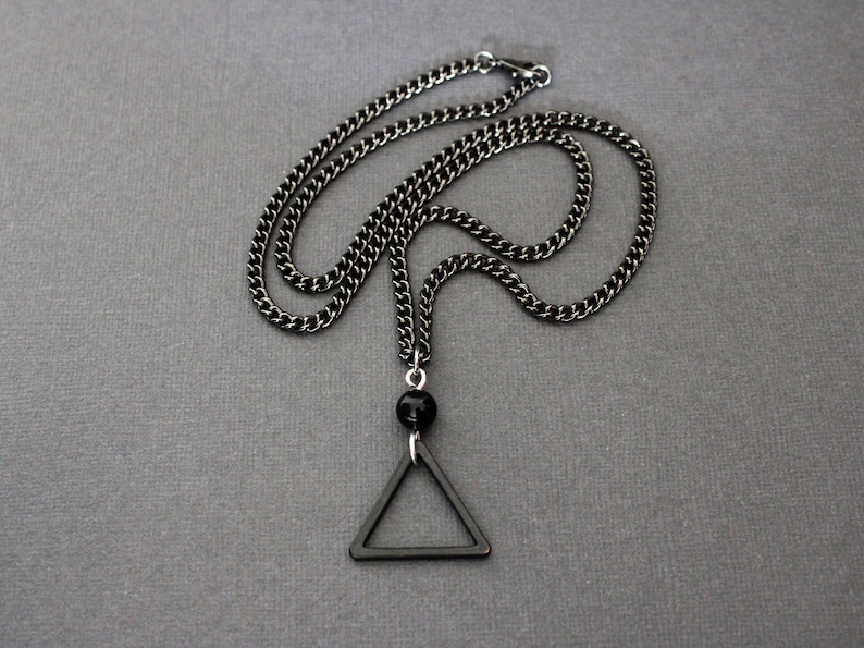 May include: A black chain necklace with a black triangle pendant and a black bead.