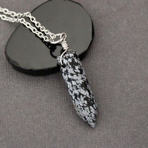 May include: A silver chain necklace with a black and white snowflake obsidian pendant. The pendant is wrapped in silver wire and has a pointed shape.
