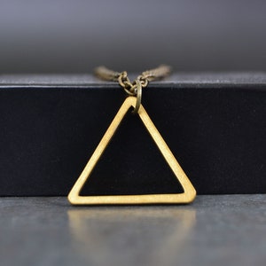 Peut inclure: Un collier avec un pendentif en forme de triangle dor&eacute; sur une bo&icirc;te noire. Le triangle est creux et a un design simple.