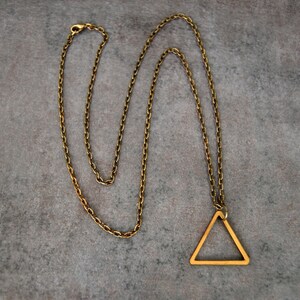 Peut inclure: Un collier en cha&icirc;ne dor&eacute;e avec un pendentif en forme de triangle. Le triangle est creux et a un design simple.