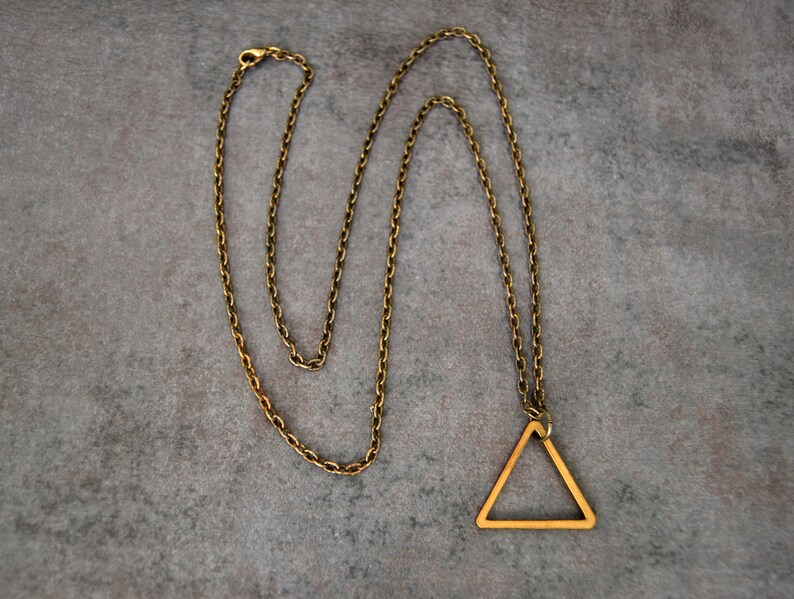 Peut inclure: Un collier en cha&icirc;ne dor&eacute;e avec un pendentif en forme de triangle. Le triangle est creux et a un design simple.