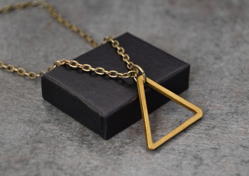 Peut inclure: Un collier en cha&icirc;ne dor&eacute;e avec un grand pendentif triangulaire ouvert. Le pendentif est en m&eacute;tal &eacute;pais et poli et pend &agrave; une simple cha&icirc;ne.