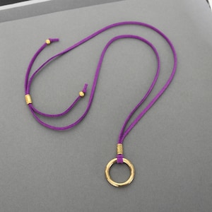 May include: A purple suede cord necklace with a gold circle pendant. The cord has gold beads at the ends.