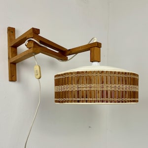 Può includere: Una lampada da parete in legno con un paralume intrecciato bianco e marrone. La lampada ha un semplice interruttore on/off sul cavo.