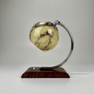 May include: A chrome and wood desk lamp with a marbled glass shade. The lamp has a curved arm and a round base.