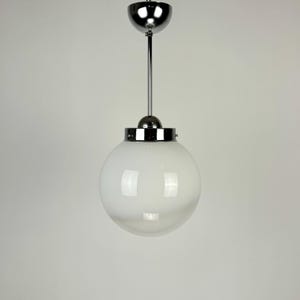 May include: A modern pendant light with a spherical, white glass shade. The light fixture has a chrome finish, including the canopy, stem, and the band around the shade. The design is simple and elegant, suitable for various interior styles.