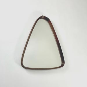 May include: A triangular-shaped wall mirror with a dark brown wooden frame. The mirror has a smooth, reflective surface and is mounted on a white wall. The frame has rounded edges.