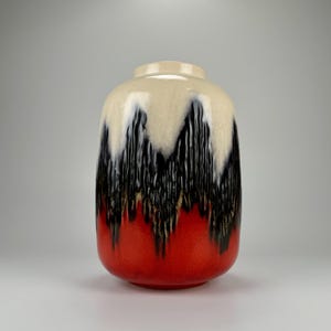 May include: A ceramic vase with a white, black, and red glaze. The vase has a rounded shape and a wide opening.