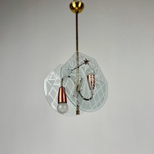 Op de afbeelding: Een moderne hanglamp van glas en messing uit het midden van de eeuw met gegraveerde glazen lampenkappen. De lamp heeft twee lampen en een koperen afwerking.