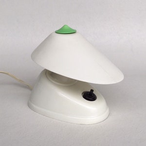 Può includere: Una lampada da tavolo bianca con un top verde e un paralume bianco. La lampada ha un interruttore nero sul lato.