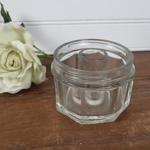 May include: A clear glass jar with a round opening and a smaller, round opening in the center. The jar has a textured, octagonal base.