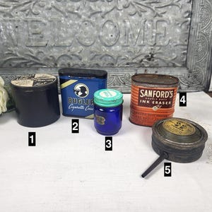 May include: Assortment of vintage tins and containers, including a blue tin labeled "Bugler Cigarette Case", a brown tin labeled "Sanford's Double Duty Ink Eraser", a blue glass jar with a green lid, a black tin with white lettering, and a round metal container with a long metal spout.