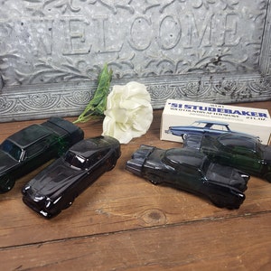 May include: Four vintage glass car shaped bottles of aftershave. The bottles are black and green and shaped like classic cars. The box is white with blue lettering and says "Avon '51 Studebaker Aftershave 2 fl. oz."