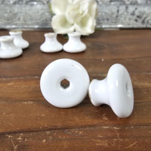 May include: A set of six white ceramic cabinet knobs with a smooth, rounded design. The knobs have a simple, classic look and would be a great addition to any kitchen or bathroom.
