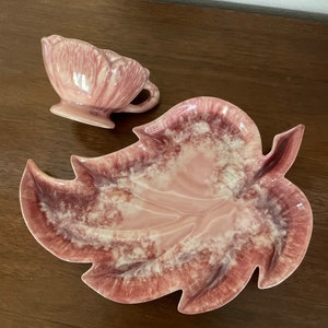 Pu&ograve; includere: Un piatto in ceramica a forma di foglia rosa e bianco con una tazza in ceramica rosa e bianco abbinata. Il piatto e la tazza hanno una glassa marmorizzata.