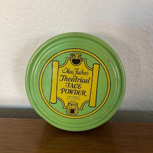 May include: A green round tin with a yellow label that reads "Max Factor's Theatrical Face Powder, Hollywood California U.S.A."