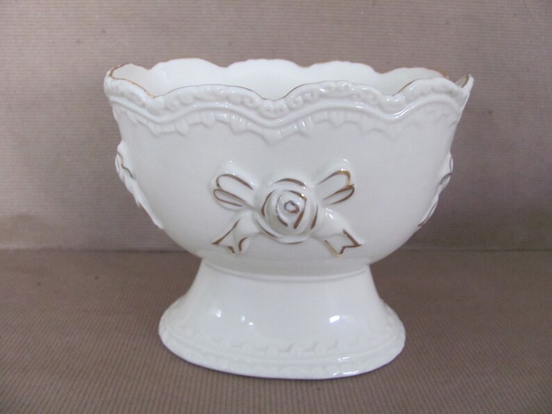 Puede incluir: Taz&oacute;n de cer&aacute;mica blanco con base de pedestal y detalles dorados. El taz&oacute;n presenta un dise&ntilde;o en relieve de una rosa con un lazo.