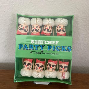 May include: A green box of 8 Gourmet Chef Party Picks. Each pick features a chef design with a white honeycomb hat, a red neckerchief, and a black mustache. The text "8 Gourmet Chef Party Picks" is printed on the box.